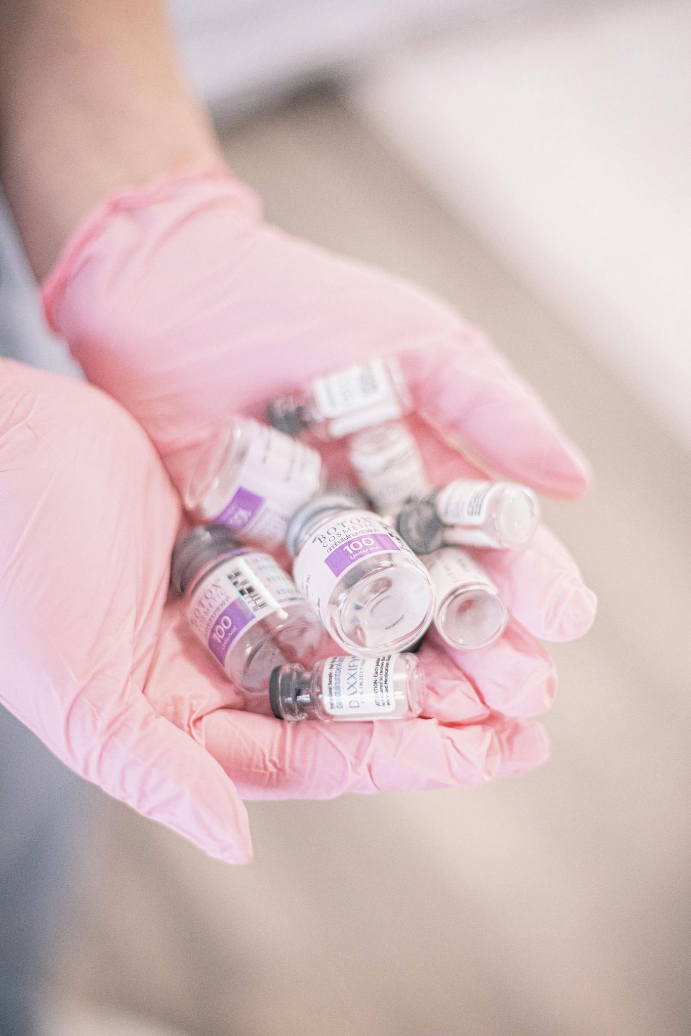 A close-up of hands in pink gloves holding vials for cosmetic treatment, suggesting skincare or medical aesthetics.